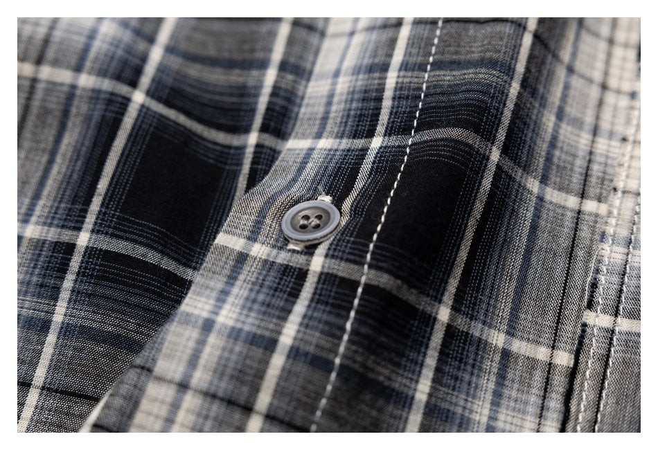 Close-up of a gray button and white topstitching on black, gray, and cream plaid fabric.