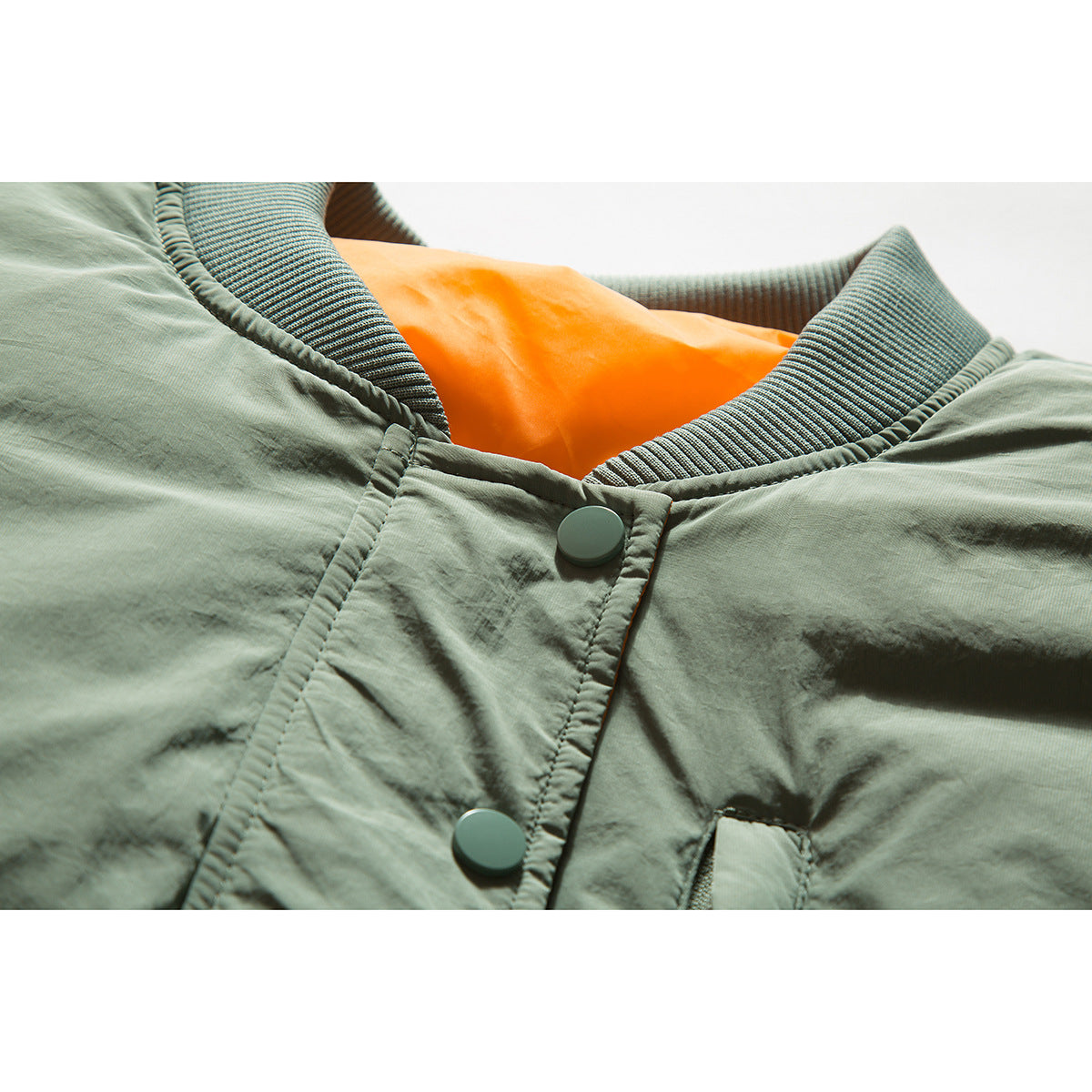 Close-up of a sage green bomber jacket collar, orange lining, ribbed trim, and snap-button placket.