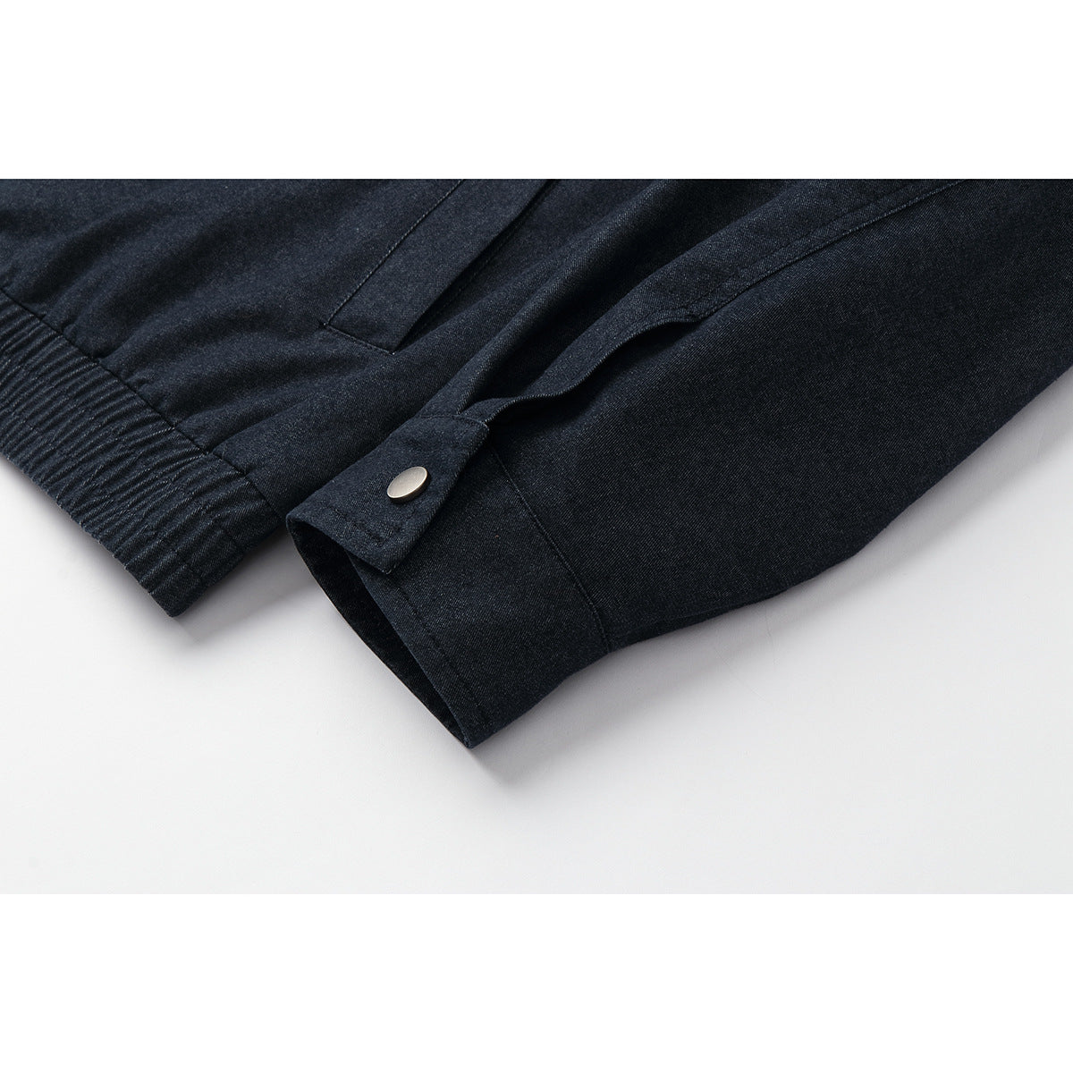Close-up of a dark indigo jacket sleeve cuff with a snap tab and ribbed edge.