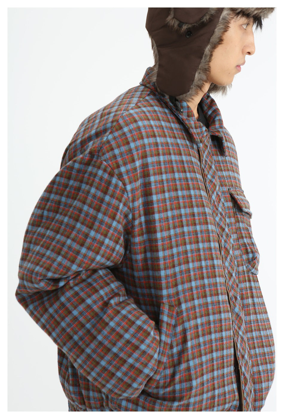 Close side view of a person wearing a blue and rust plaid jacket and a brown fur-trimmed trapper hat.