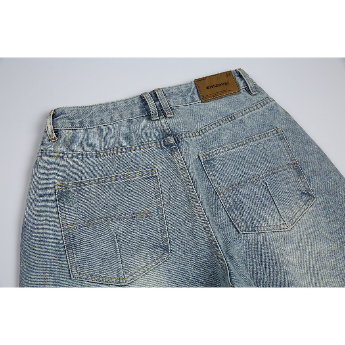Close-up of the back waistband and two patch pockets on light blue washed jeans.