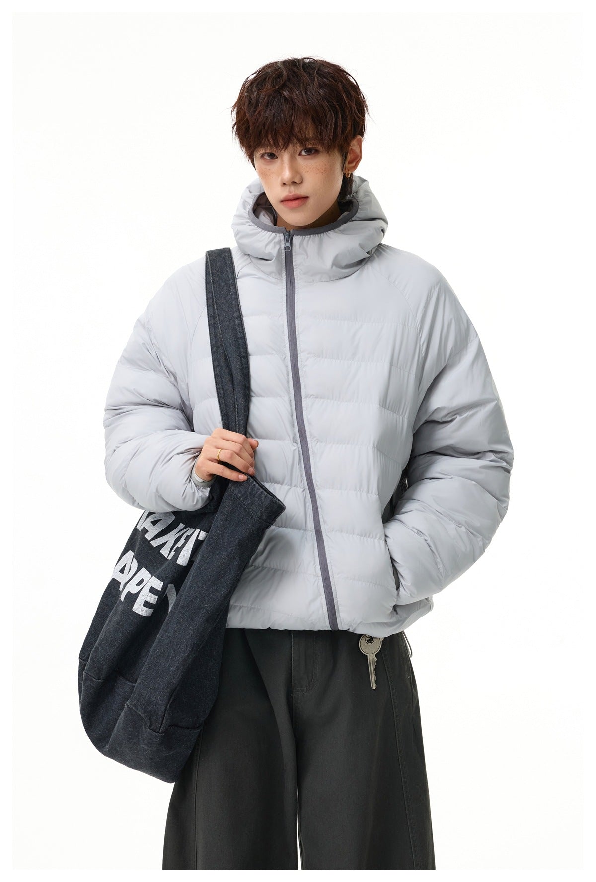 Model wearing a light gray quilted hooded jacket with gray zipper trim, carrying a dark tote bag.