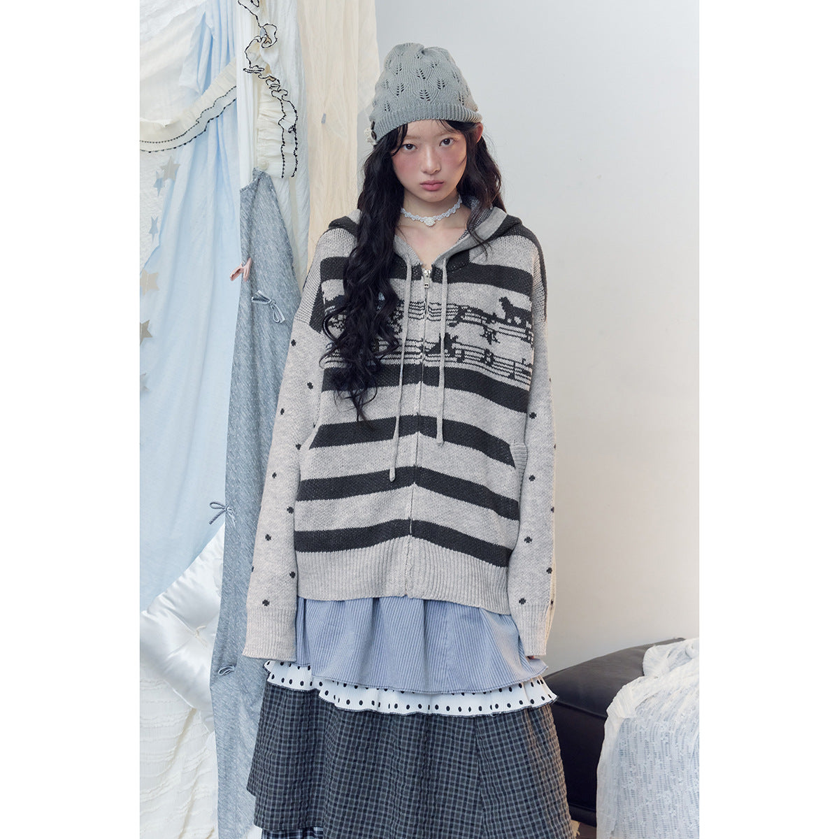 Model wearing a gray-and-black striped hooded sweater with dotted sleeves, a gray beanie and a layered skirt.