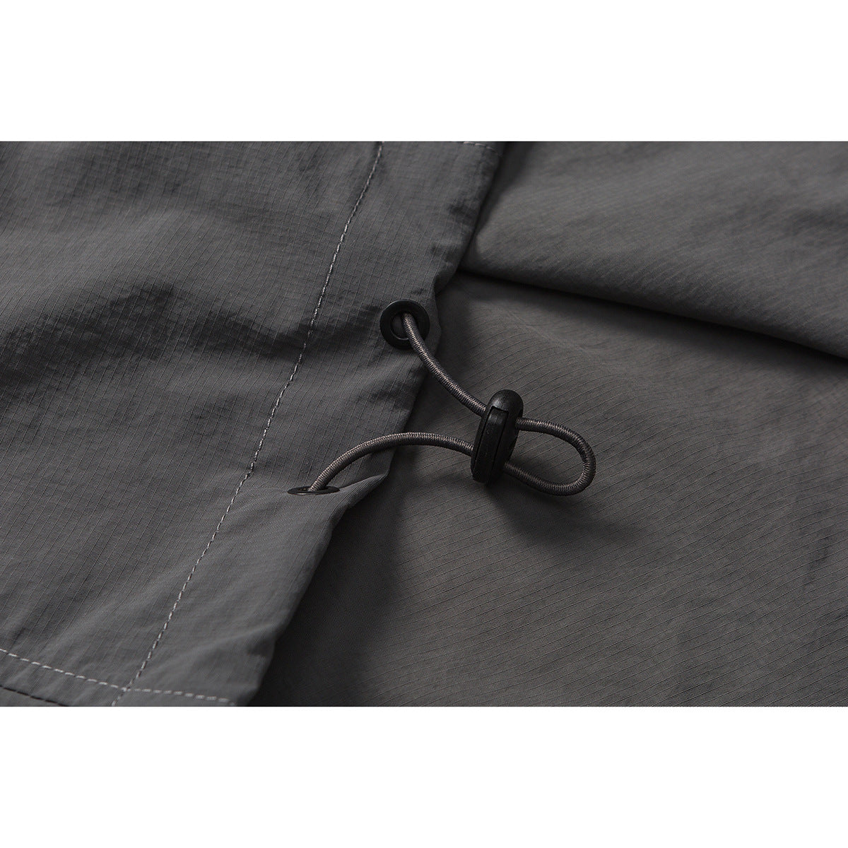 Close-up of a charcoal gray garment's hem drawcord and black cord lock.