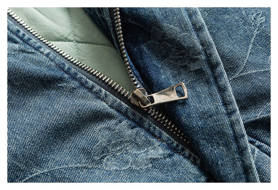 Close-up of an open metal zipper on a blue denim garment with tonal stitched motifs.