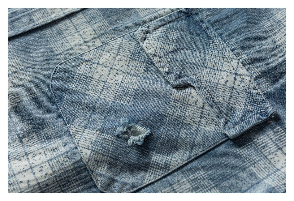 Close-up of a chest pocket on blue-gray patterned denim with a buttoned flap and distressed tear.