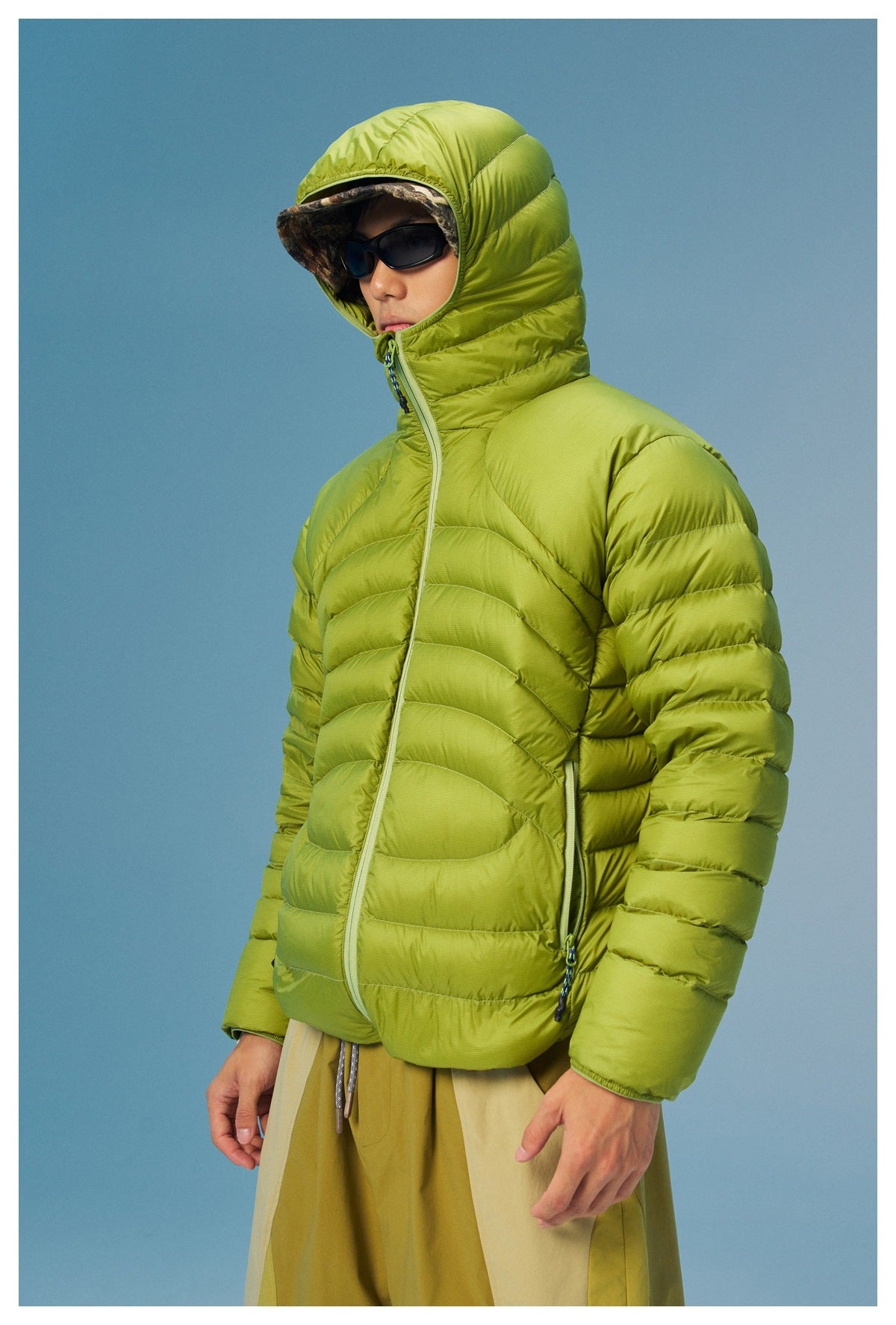 Model wearing a lime-green quilted jacket with the hood raised and zipped high around the face.