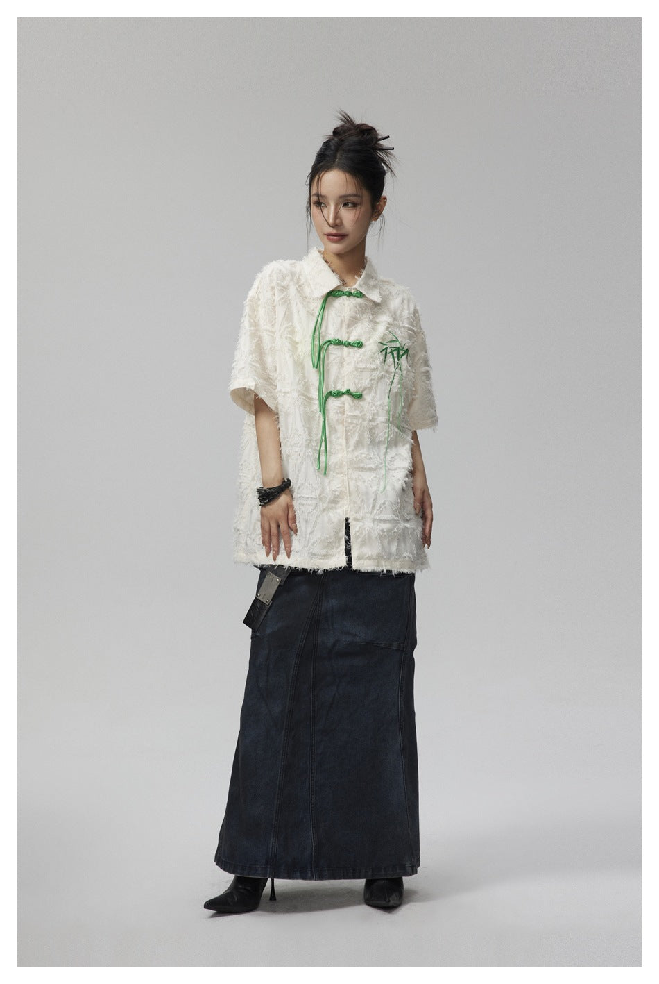Full-length model wearing an ivory textured jacket with green frog closures and a dark denim maxi skirt.
