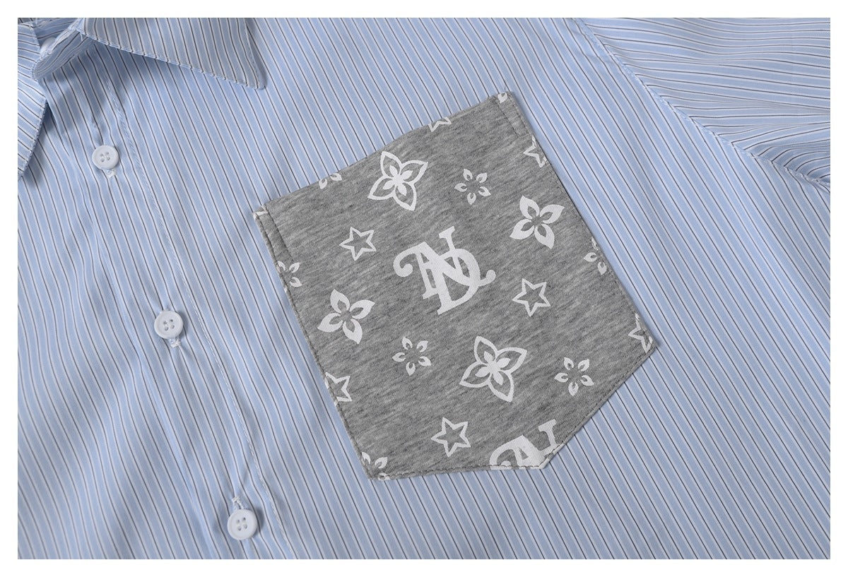 Close-up of a light blue pinstriped shirt with a gray pocket printed with flowers, stars, and a monogram.