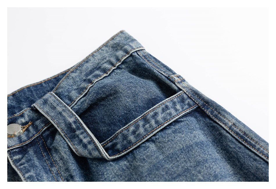 Close-up of a large angular front pocket and belt loop on blue distressed denim jeans.