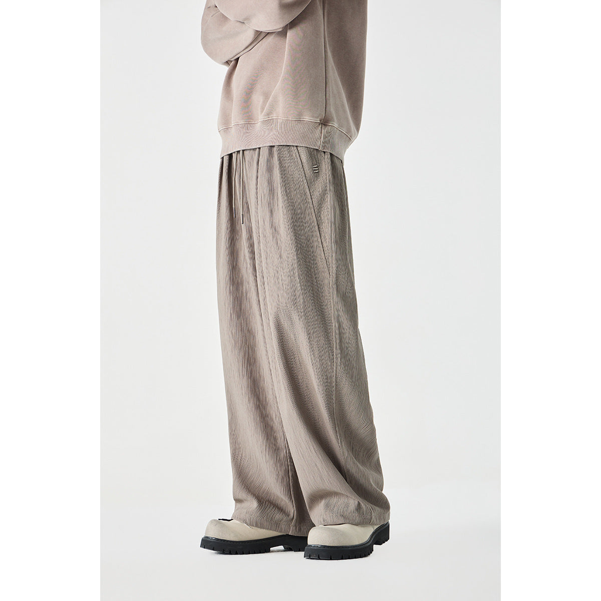 Side view of taupe wide-leg drawstring pants worn with a matching sweatshirt and light shoes.