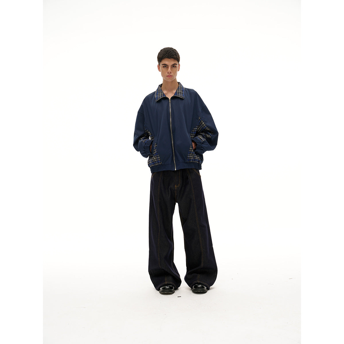 Front view of a model wearing a navy zip-front jacket with plaid collar and panels, and wide black jeans.