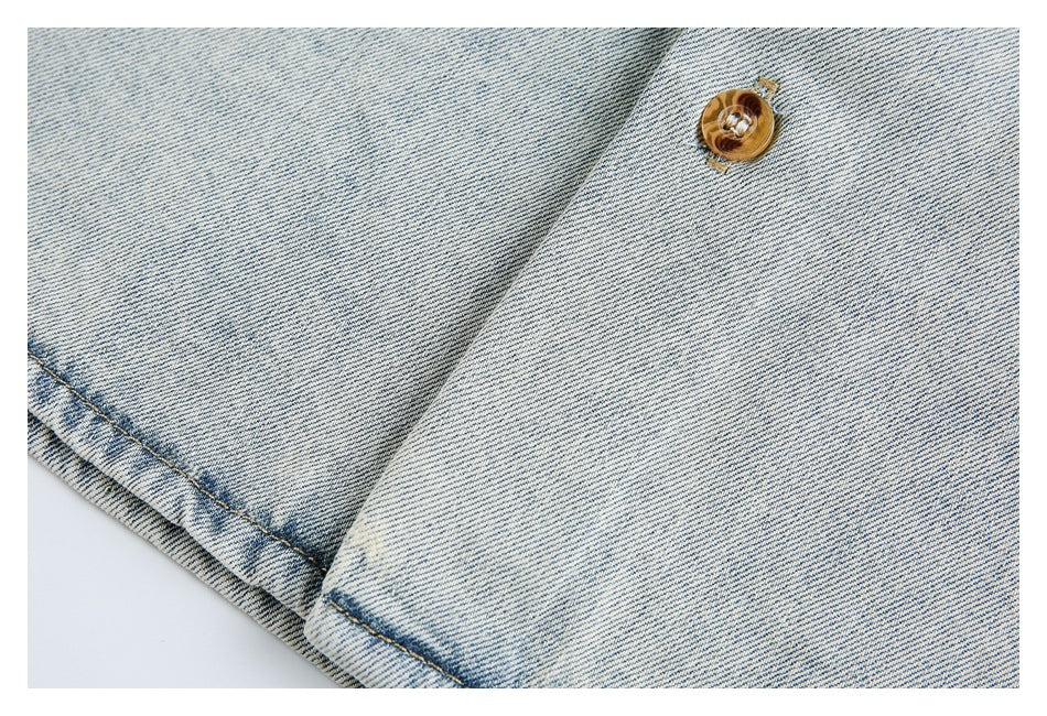 Close-up of a brown button, overlapping denim panels, and stitched hem on pale washed denim.