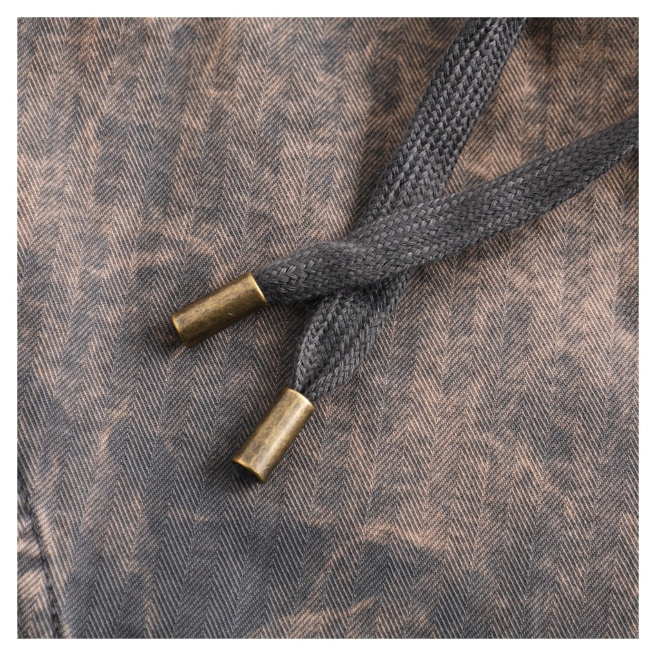 Close-up of two black braided drawstrings with brass-tone tips against brown-gray patterned fabric.