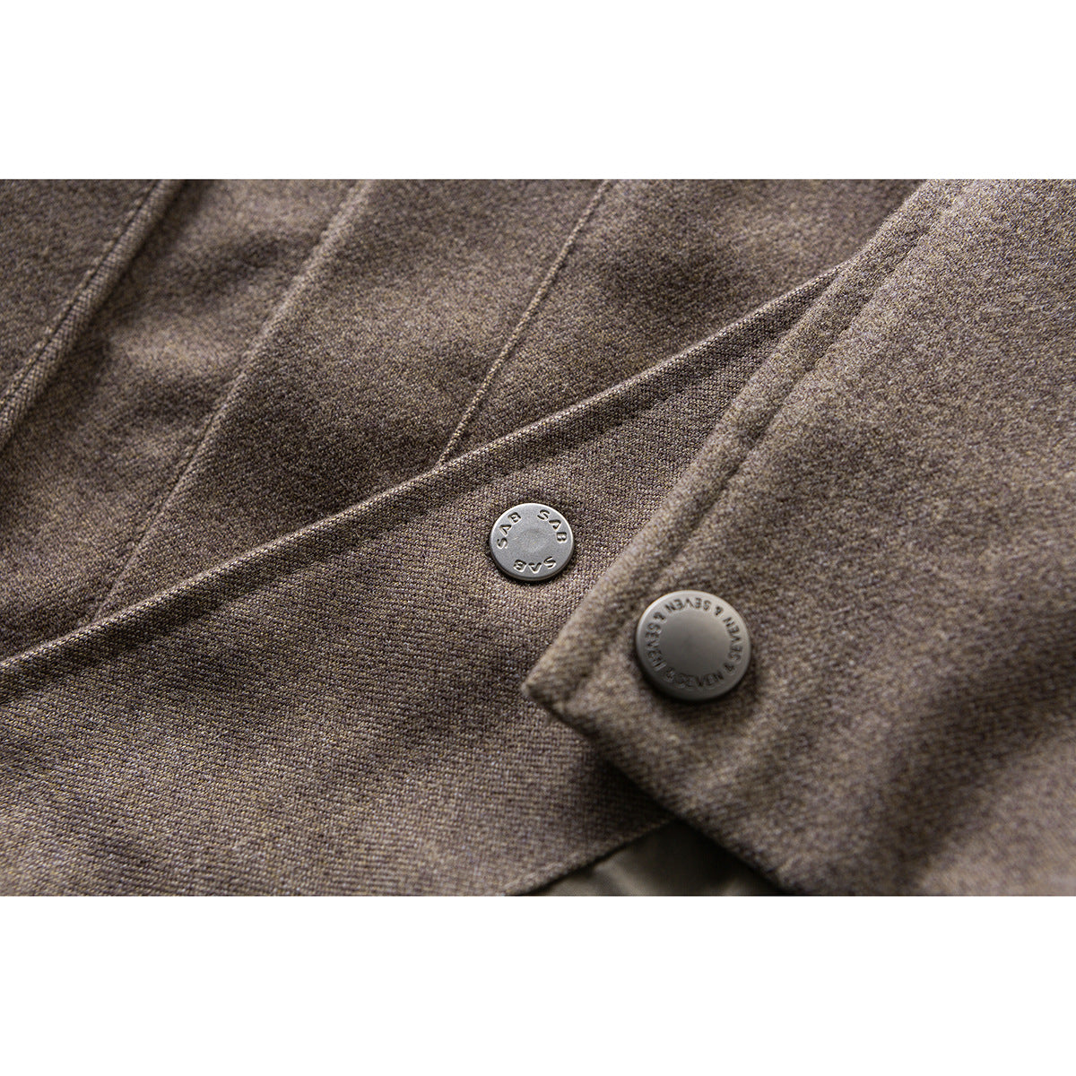Close-up of two engraved buttons and stitched seams on a taupe-brown jacket.