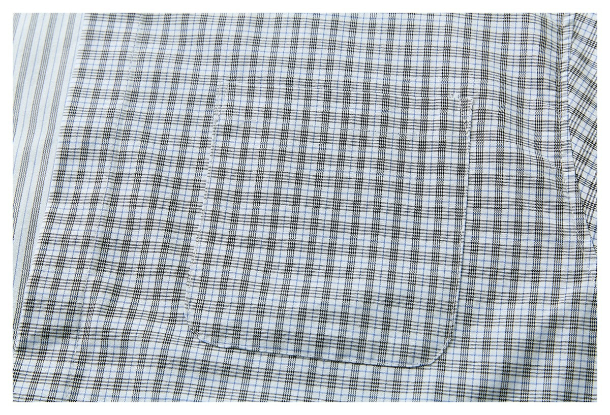Close-up of a white shirt with a black and pale blue plaid chest pocket and matching striped fabric at the edge.