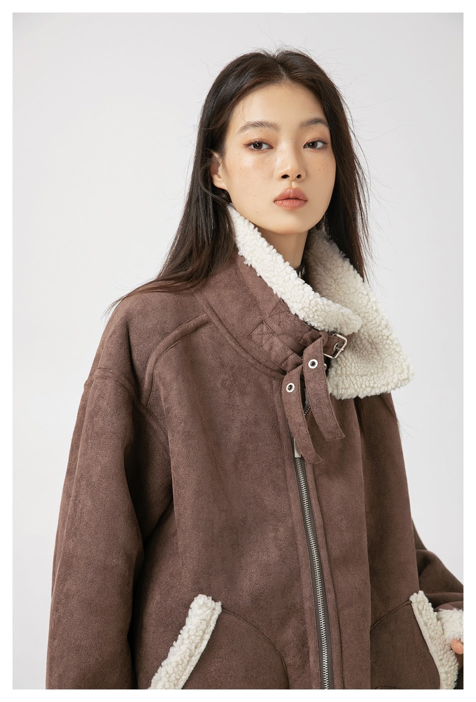 Close-up of a model in a brown jacket showing its cream sherpa collar, buckle detail and front zipper.