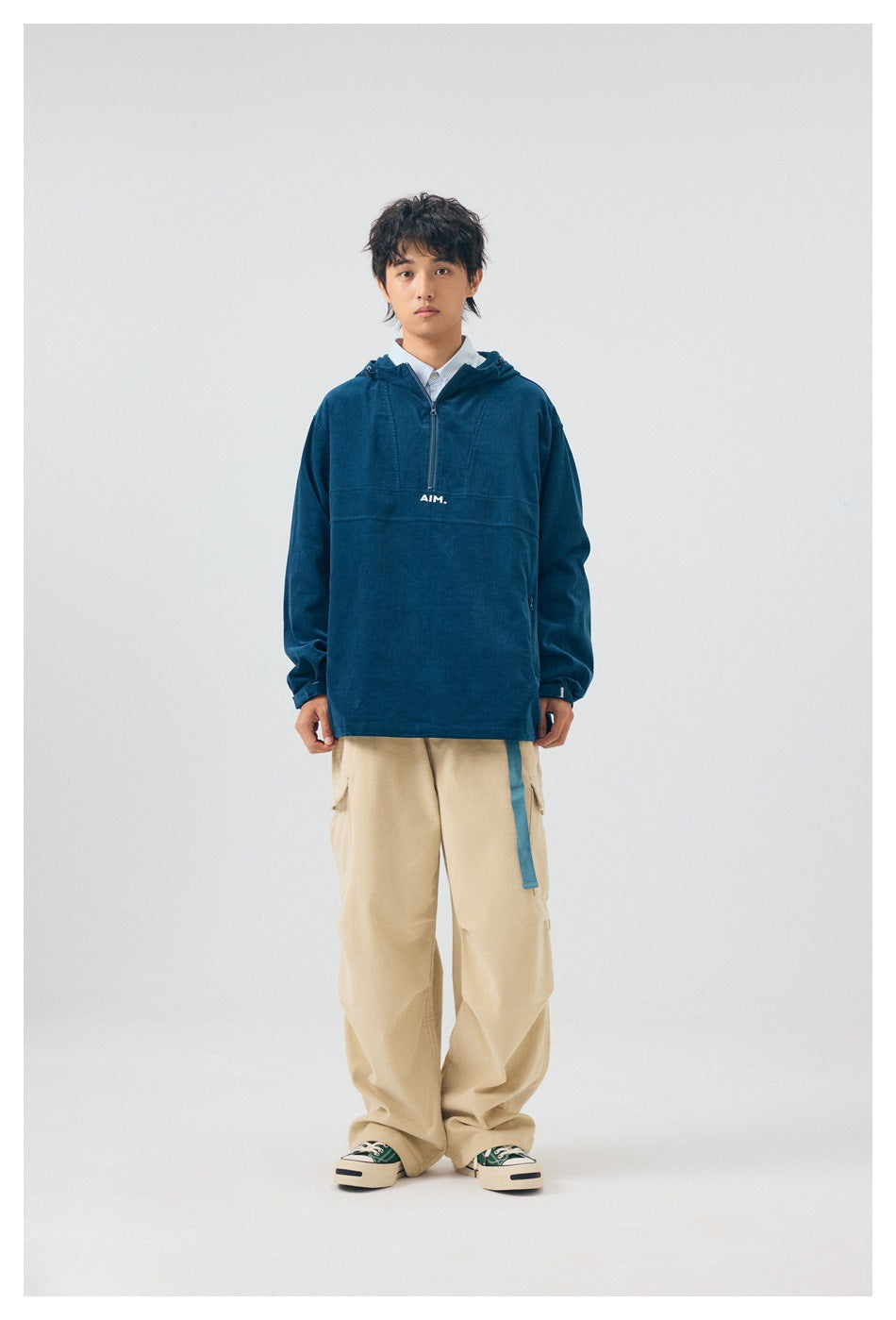 Model wearing blue hooded half-zip corduroy-style jacket with beige cargo pants, standing front view