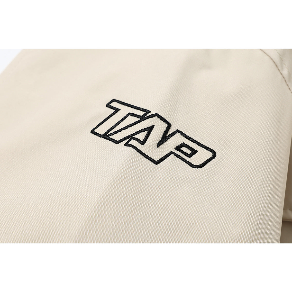 Close-up of a black outlined embroidered logo on a light beige jacket.