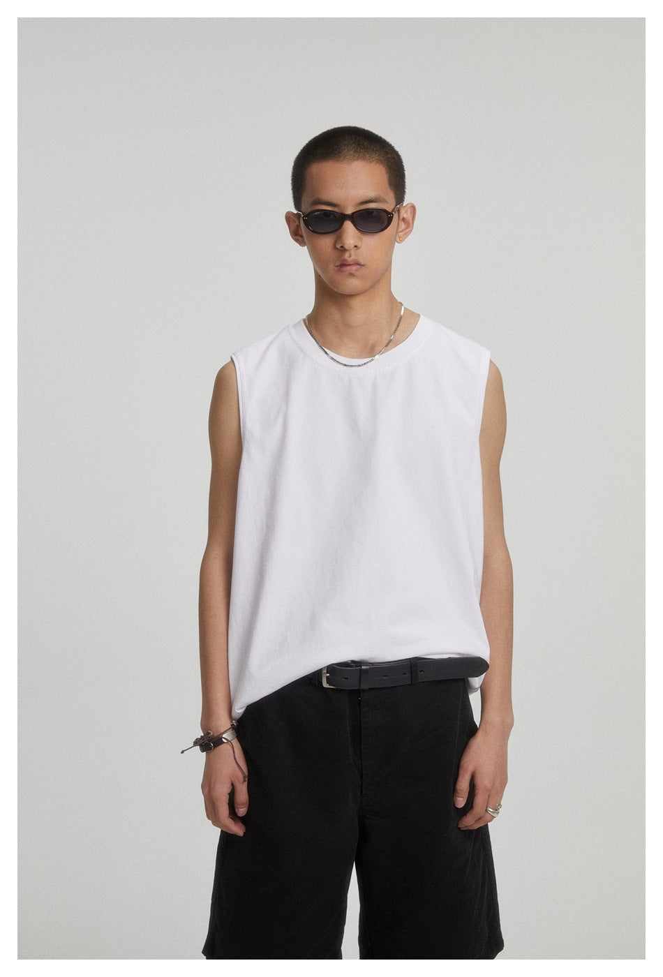 Front view of a model wearing a plain white sleeveless crew-neck shirt and black shorts.