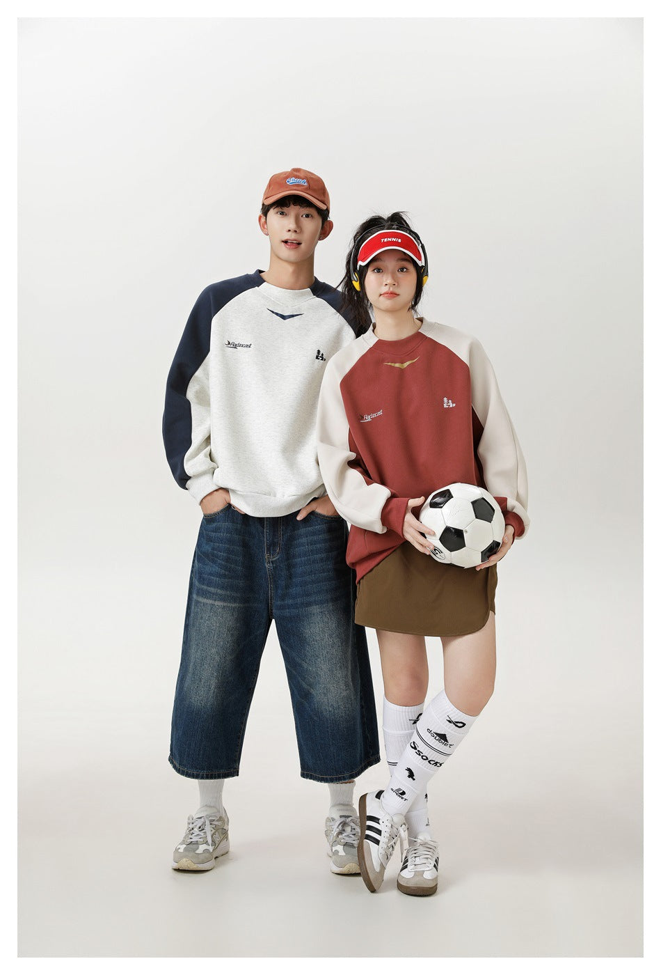 Two models wear color-block raglan sweatshirts, one gray and navy and one rust and cream; the woman holds a soccer ball.