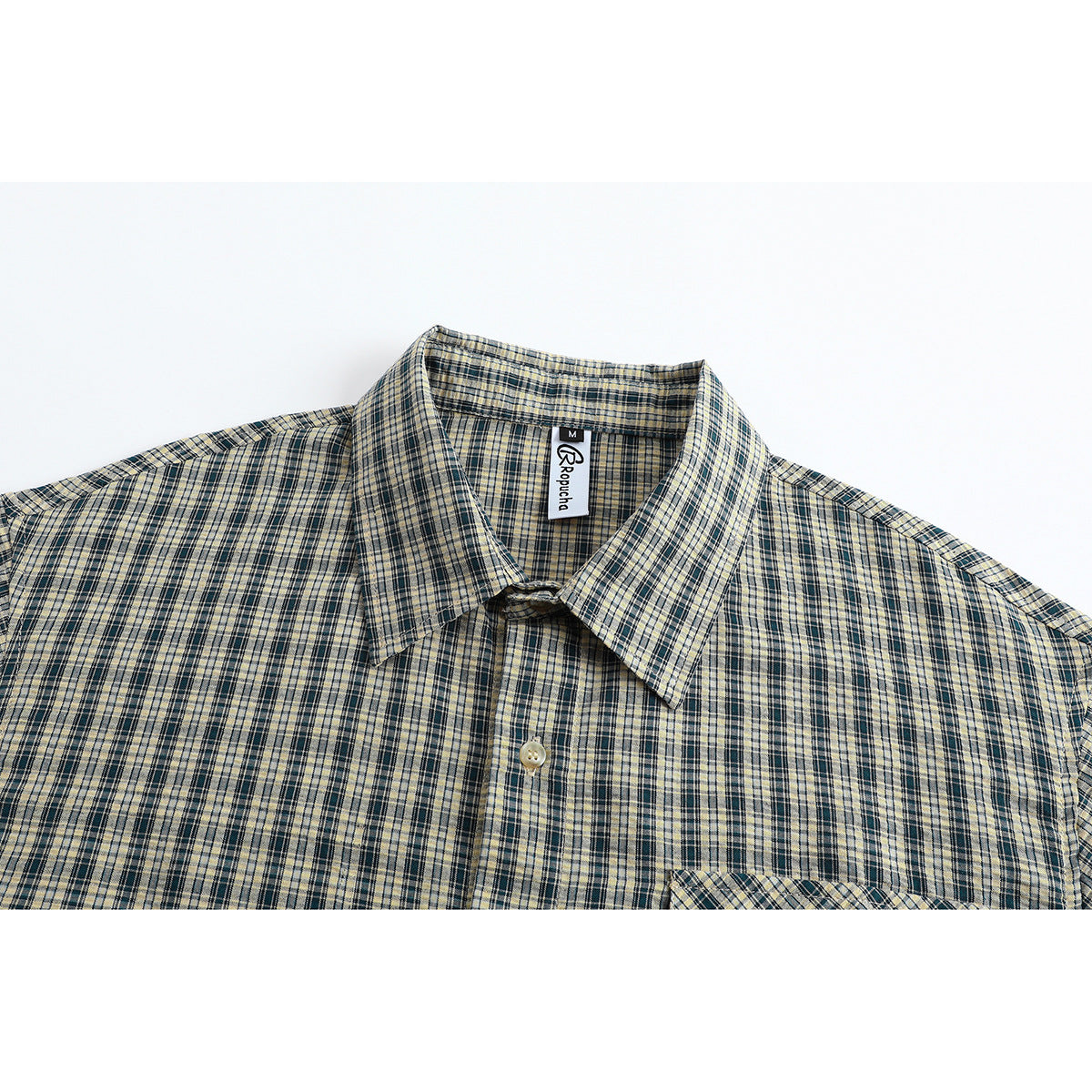 Close view of a beige, navy, and gray plaid shirt collar, upper chest, and partial pocket.