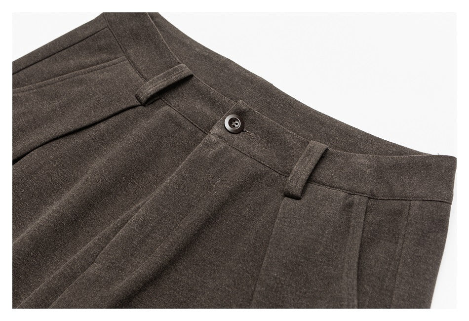 Close-up of brown trouser waistband showing the button, belt loops, pleats and pocket opening.
