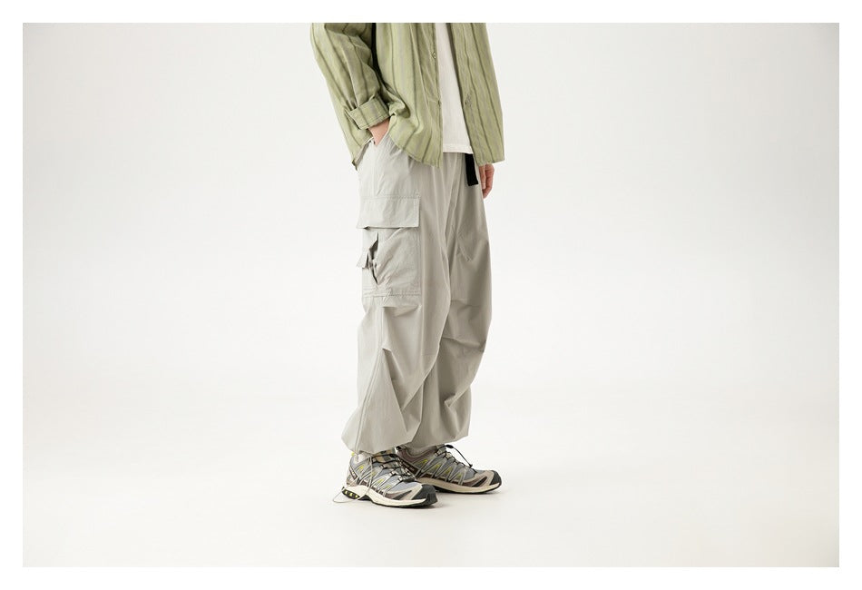 Side view of a cropped model wearing loose light gray cargo pants with stacked flap pockets.