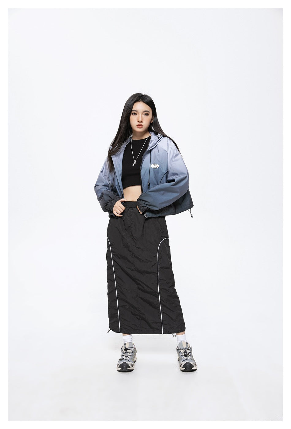 Model in a blue-gray hooded zip jacket and black ankle-length skirt with white piping.