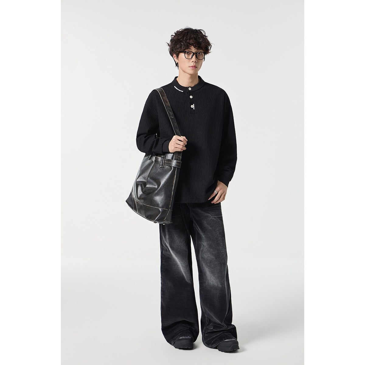 Model wearing a black ribbed Henley with dark wide-leg jeans and carrying a black shoulder tote.