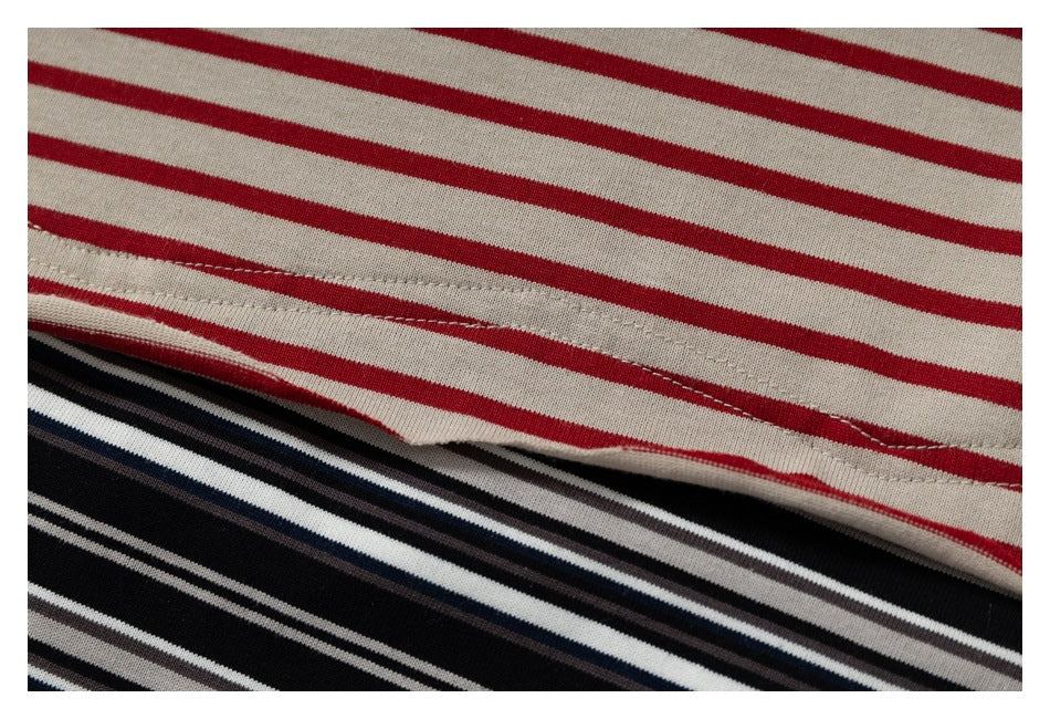 Close-up of cream fabric with red stripes layered over black, white, and navy striped fabric, showing a stitched edge.