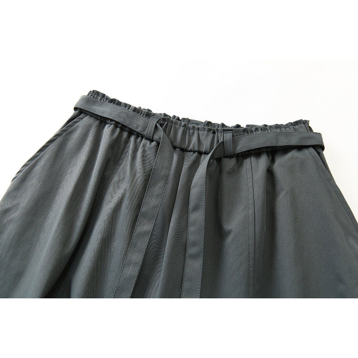 Close-up of charcoal-gray wide-leg trousers showing the gathered waistband, belt loops, and long tie belt.
