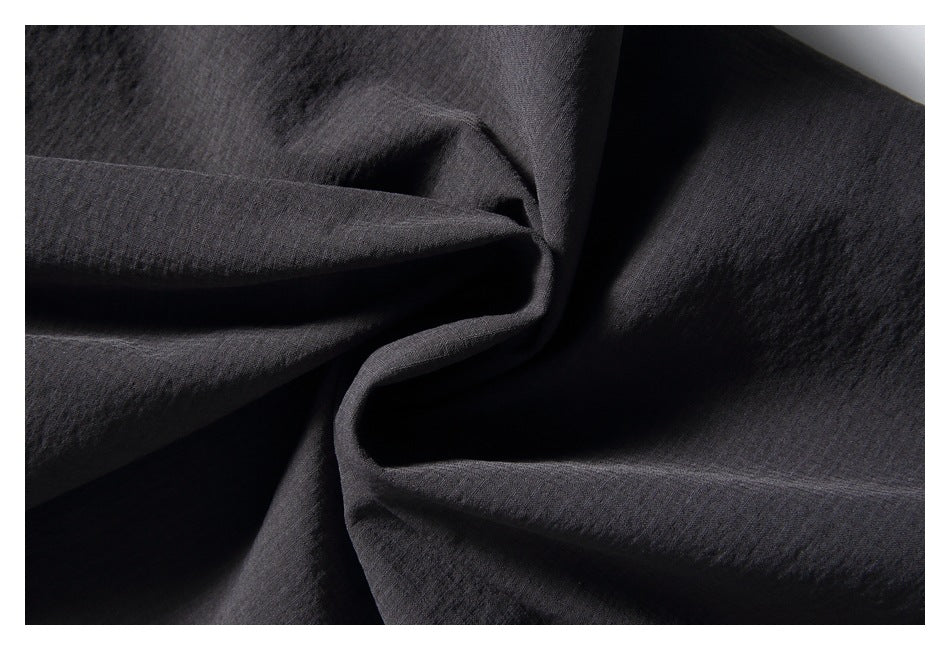 Close-up of dark charcoal fabric arranged in soft folds, showing its subtle textured surface.