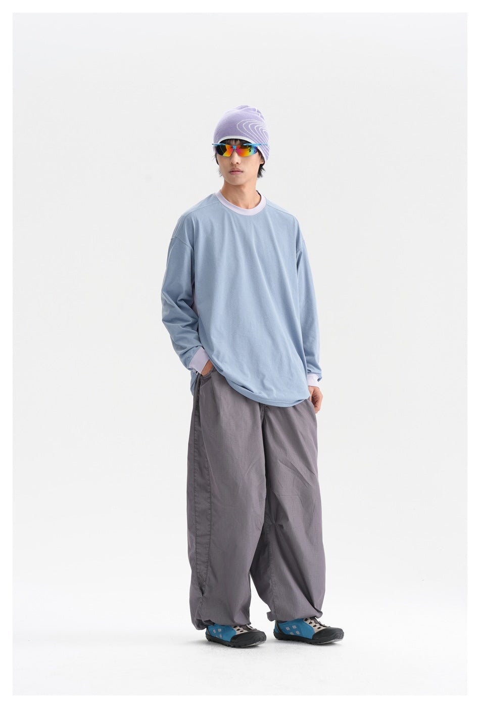 Three-quarter view of a model wearing a light-blue long-sleeve top with lavender trim and loose gray trousers.