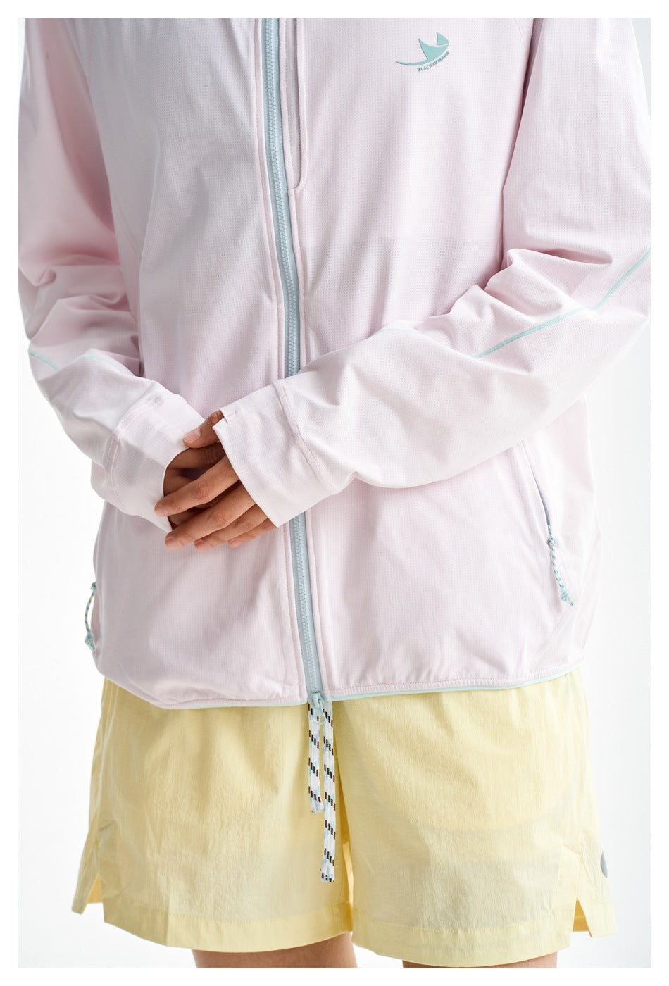 Close-up of a pale pink jacket with an aqua zipper and sleeve piping, worn with yellow shorts.