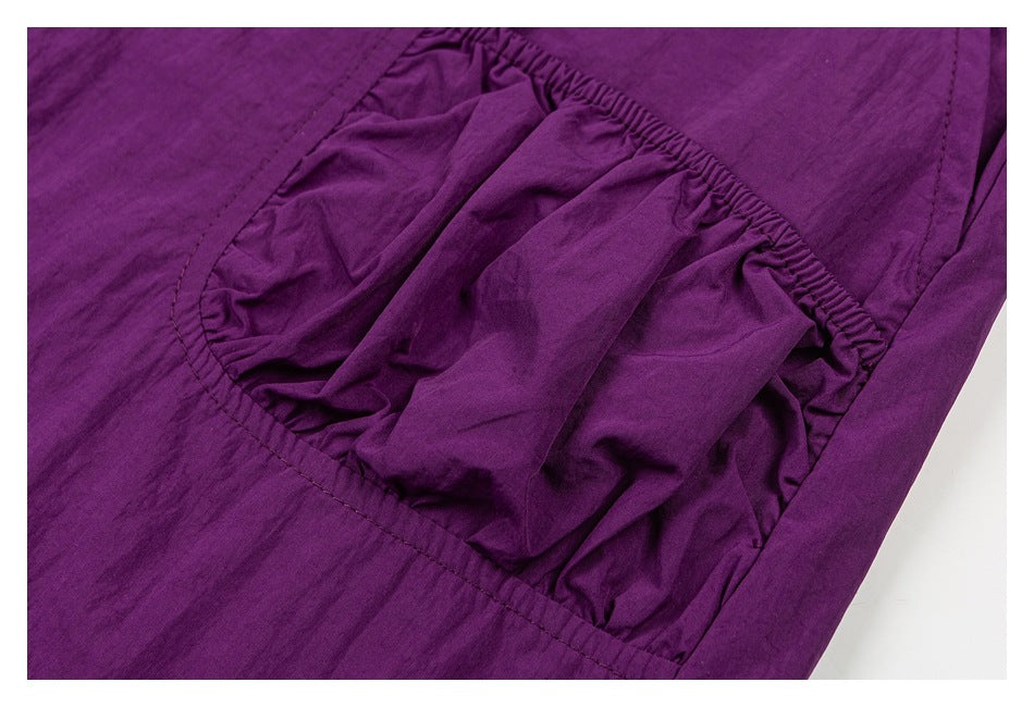 Close-up of a gathered pocket on purple pants, showing its curved stitched opening.