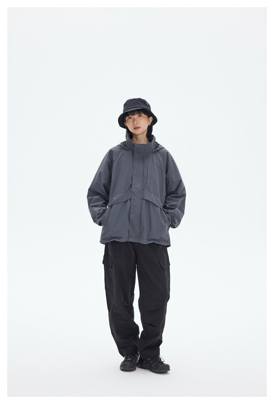 Model wearing a gray hooded jacket, black cargo pants and a black bucket hat.