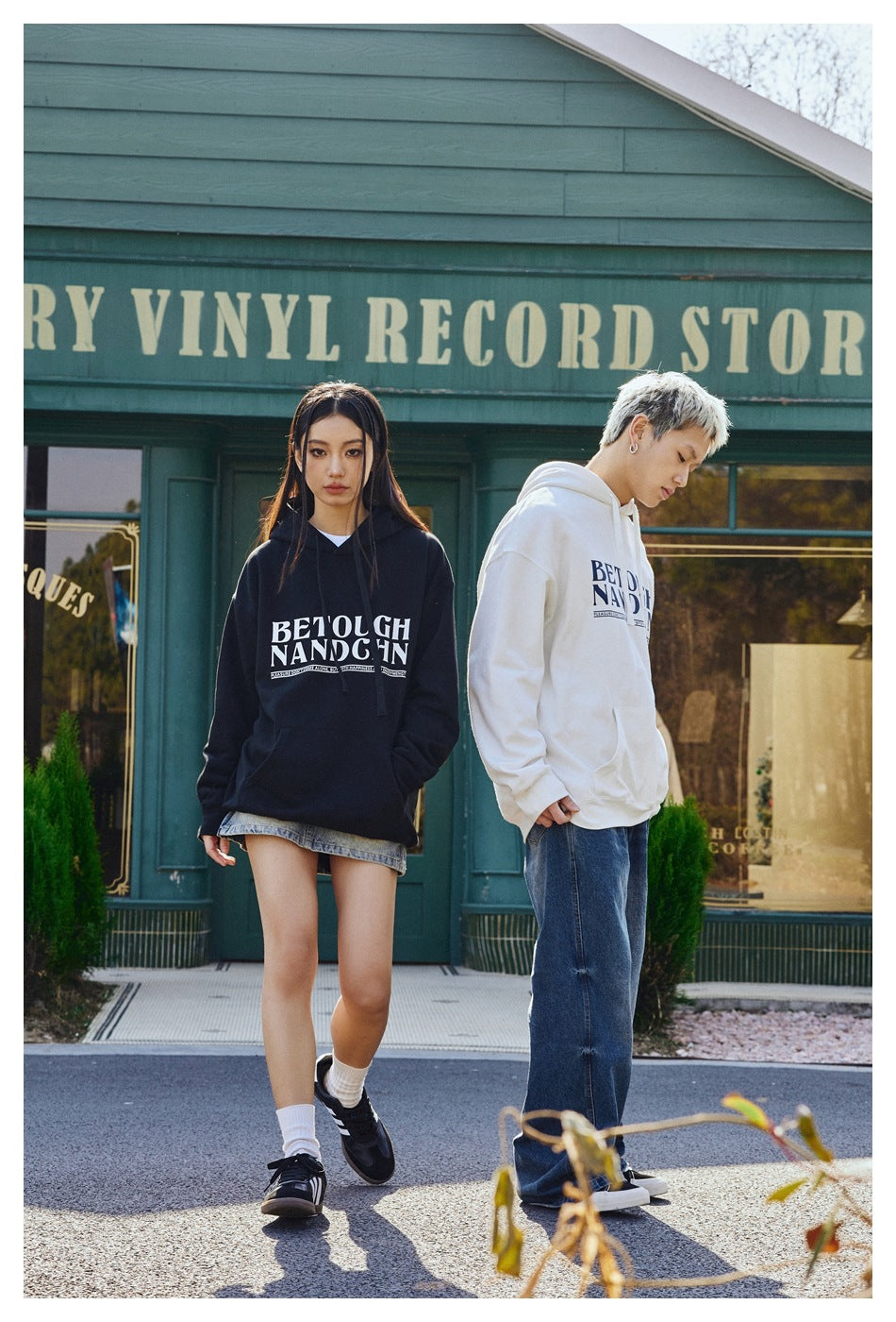 Models wear black and white graphic pullover hoodies; the black hoodie is shown from the front and the white hoodie at an