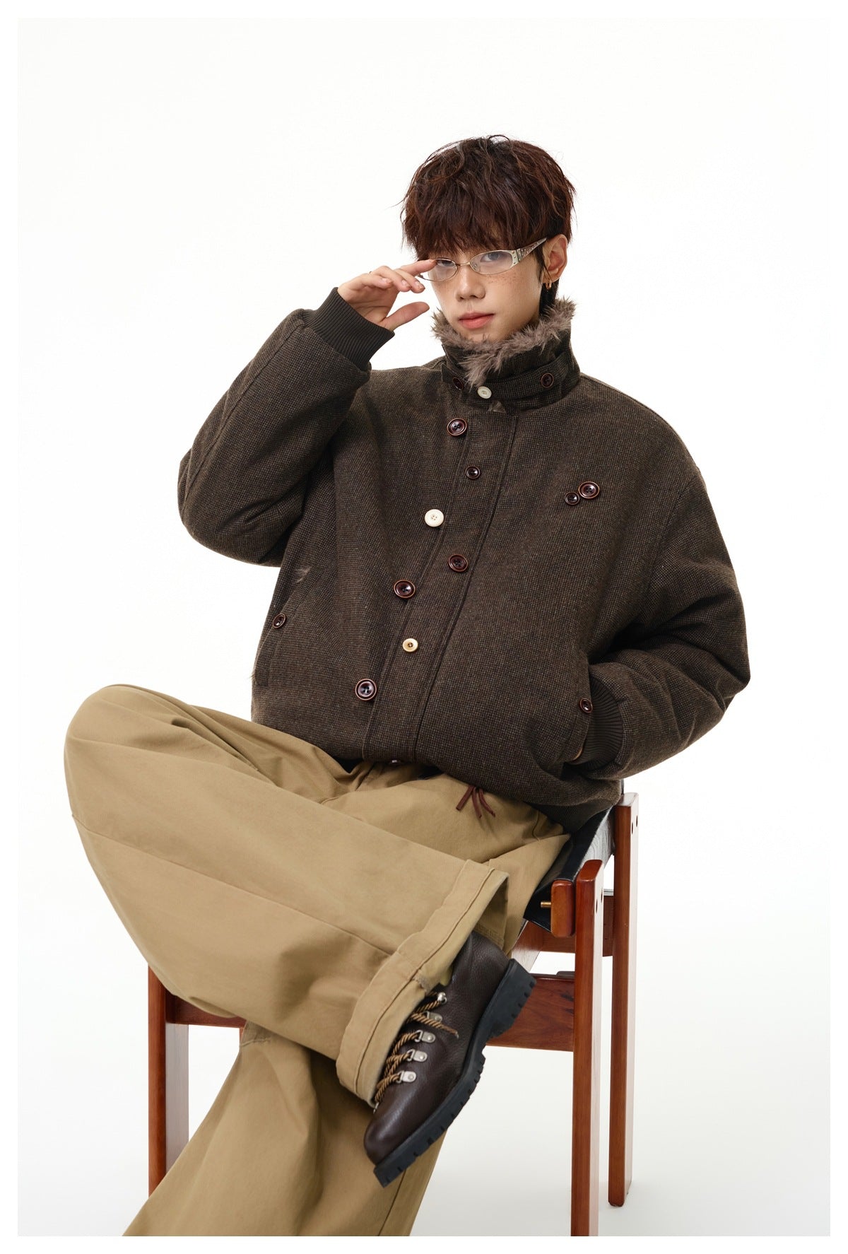Seated model wearing a dark brown textured jacket with a raised faux-fur collar and contrasting buttons.