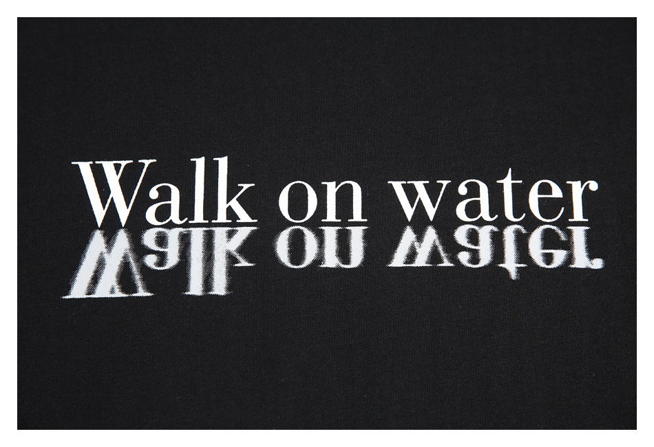 Close-up of a black garment with white “Walk on water” lettering and a mirrored reflection effect.