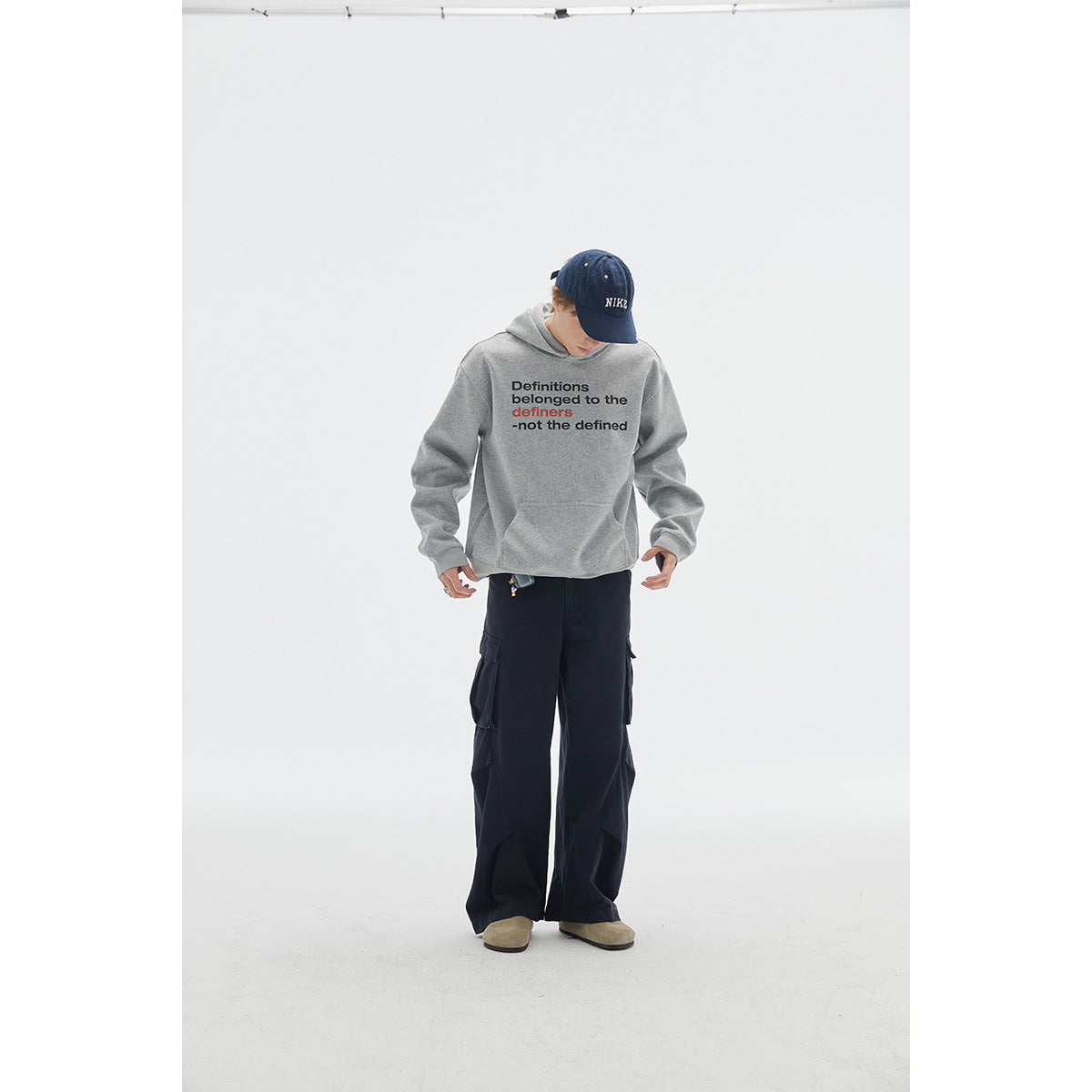 Model wearing a gray slogan-print pullover hoodie with a front pocket and dark cargo pants.