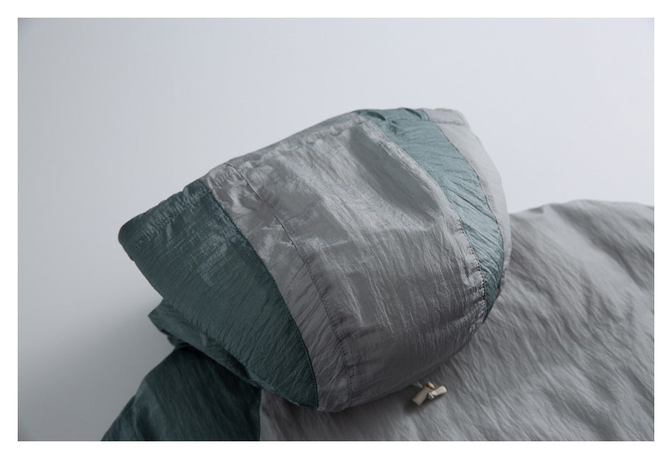 Close-up of a gray and teal garment hood with contrasting color panels and a drawcord toggle.