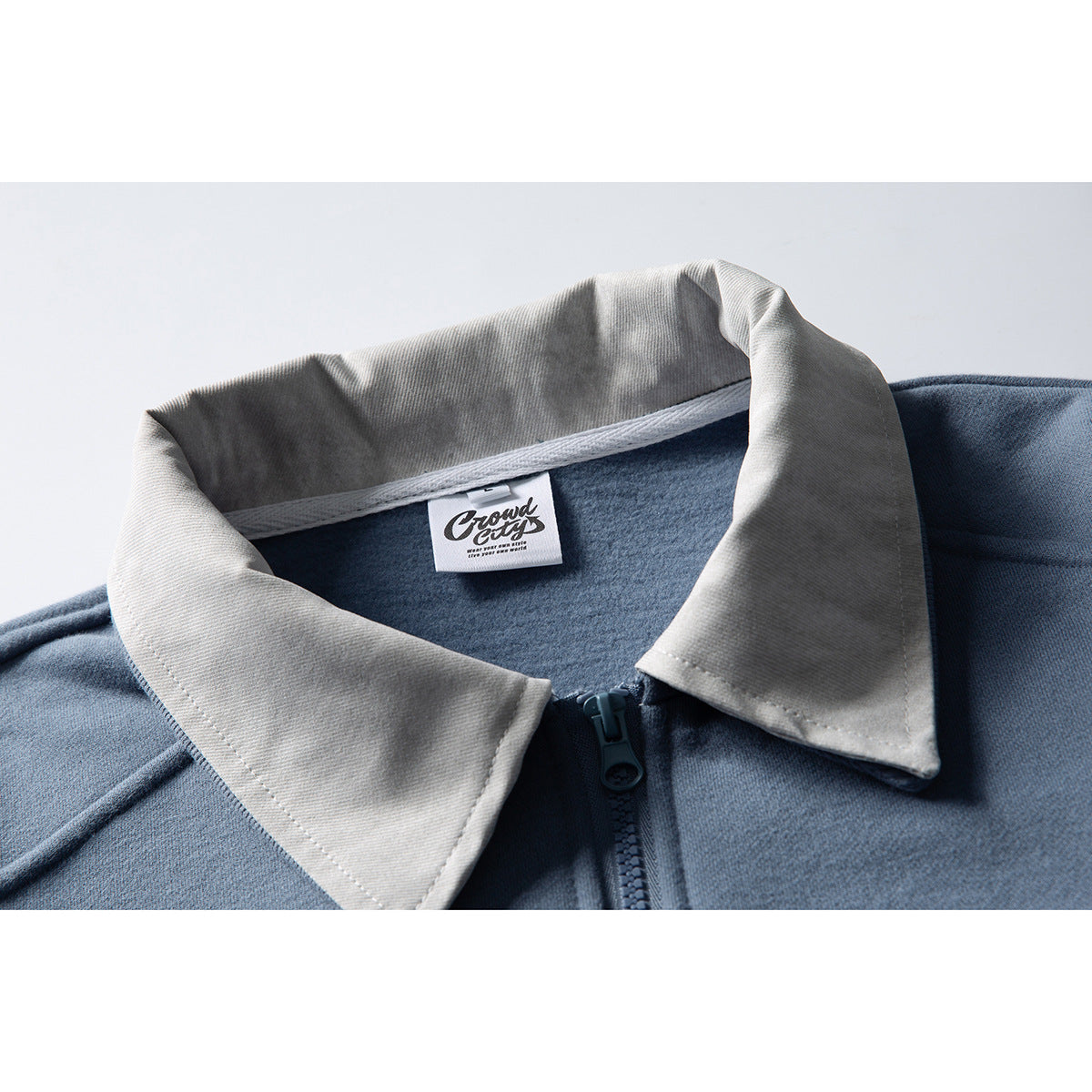 Close-up of a blue zip-up jacket with a contrasting light gray pointed collar and visible inner label.