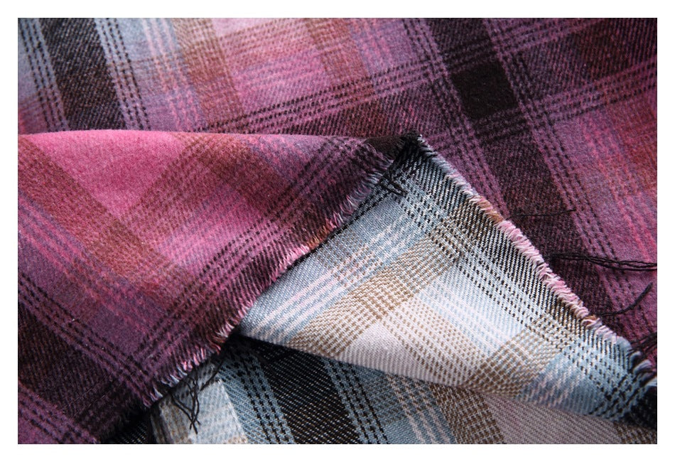 Close-up of folded plaid fabric in plum, pink, black, blue-gray, and beige, showing its woven pattern and fringed edge.