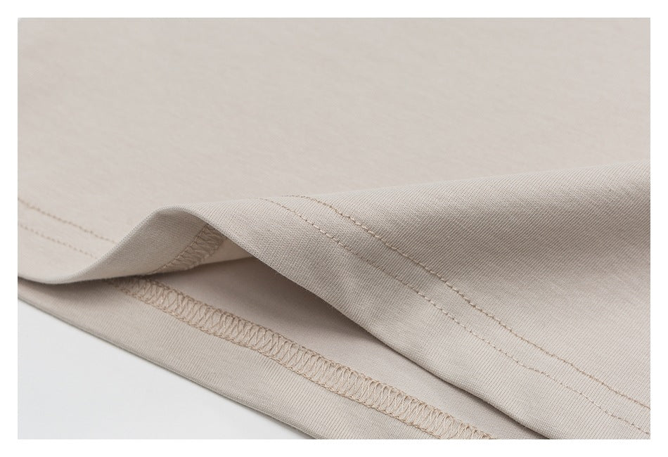 Close-up of a beige garment hem showing folded fabric and stitched seams.