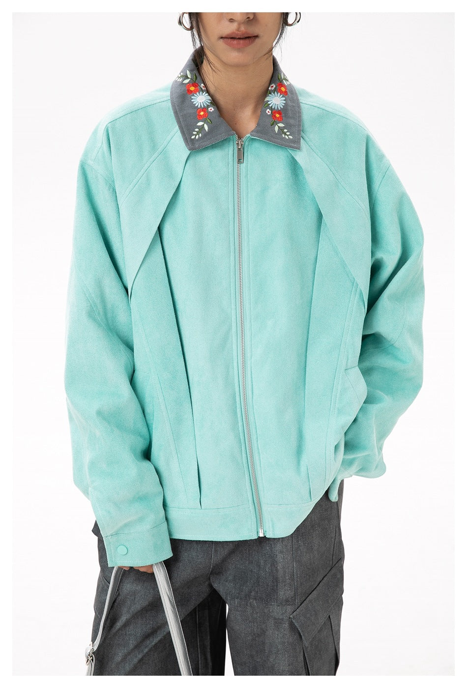Close-up of a mint jacket showing its silver zipper, gray collar with colorful floral embroidery, and front seams.
