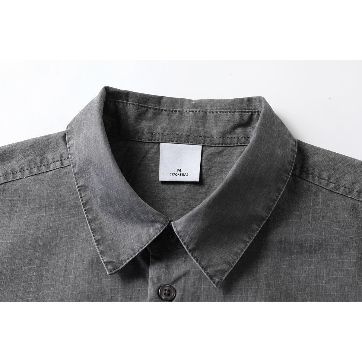 Close-up of a charcoal gray short-sleeve shirt collar, button, and inner size label.