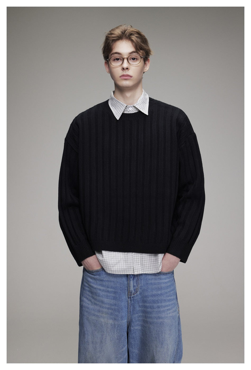 Front view of a model wearing a black ribbed sweater over a checked shirt and blue jeans.