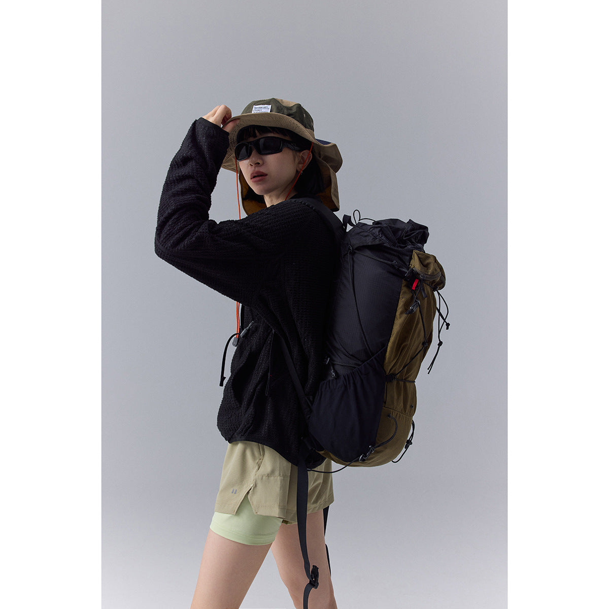 Model wearing a black textured jacket with a large hiking backpack, shown from the side.