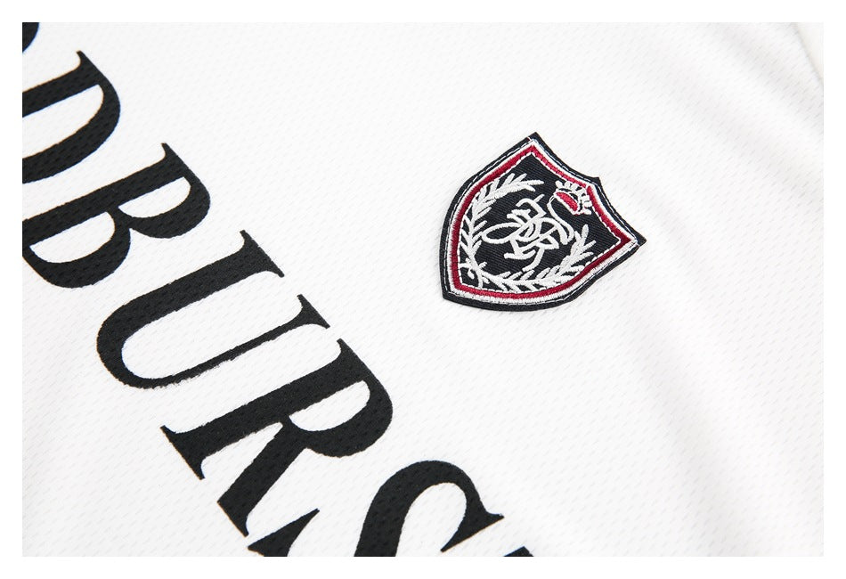 Close-up of white mesh jersey fabric with a black, red and white embroidered crest and large black lettering.